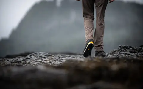 Choosing hiking boots is key for a good trek. This person walks on rocky terrain, showing off their sturdy footwear.