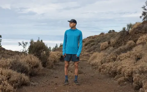 Runner in blue shirt and shorts on a dusty trail, contemplating the disadvantages of merino wool, like its tendency to hold moisture in humid conditions.