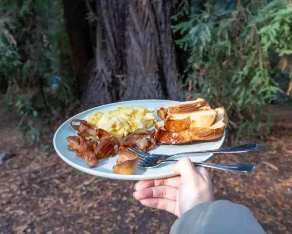 A plate of scrambled eggs, crispy bacon, and toasted bread, a delicious breakfast showcasing some great camping hacks for enjoying a hearty meal outdoors.