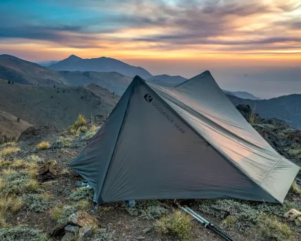 A Gossamer Gear tent sits on a rocky mountain ridge at sunset. This review highlights the gear's performance.