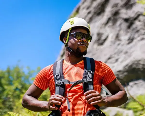 A man in a helmet and sunglasses pauses during a hike in hot weather, ready for his next climb.