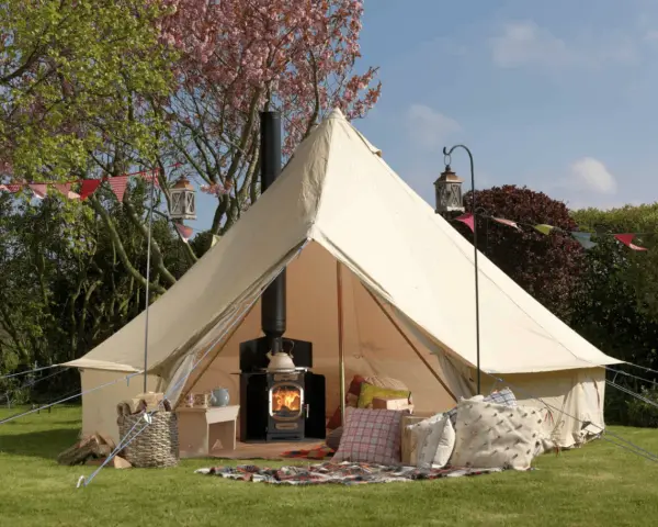 A cozy bell tent with a wood-burning stove inside, showcasing what is glamping: comfort and nature combined.