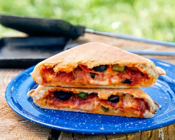 A delicious pie iron pizza, cut in half and stacked, reveals melted cheese, pepperoni, olives, and peppers.
