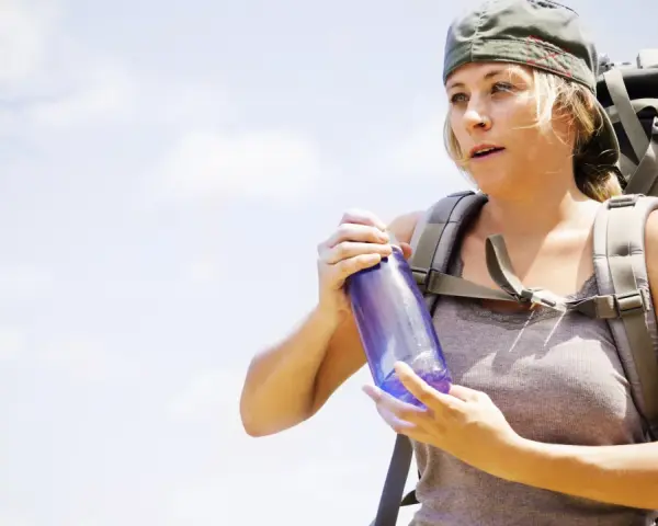 A hiker with a backpack holds a water bottle, demonstrating how to carry water while hiking.