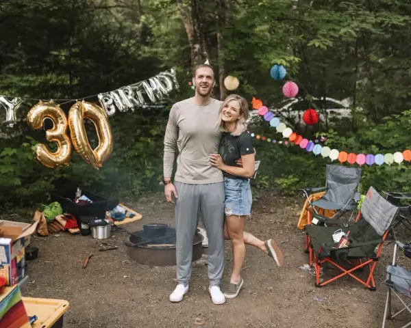 Couple celebrates 30th birthday with fun camping birthday ideas. Balloons and colorful banners decorate the campsite.