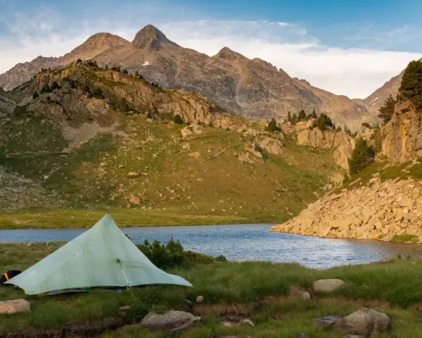 A tent sits by a serene lake, with rugged mountains in the background, a perfect campsite on the Pyrenees High Route.