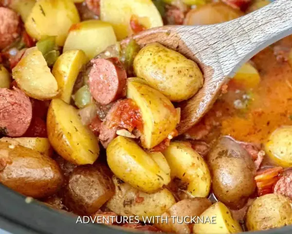 A wooden spoon scoops up hearty potatoes and sausage from a crockpot, perfect for camping crockpot meals.