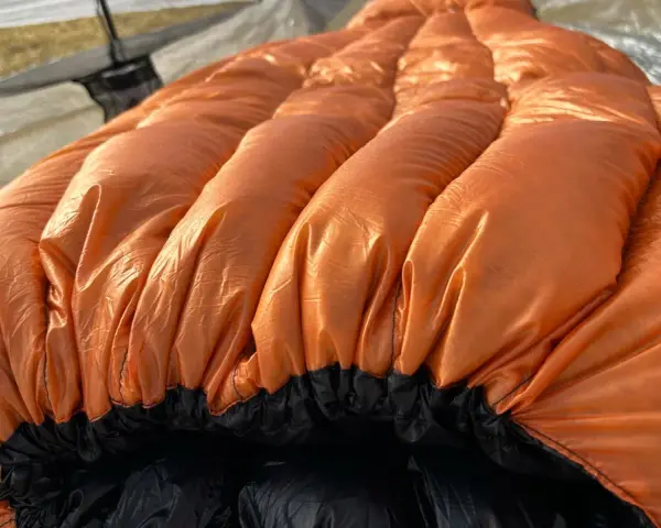 A bright orange sleeping bag with puffy baffles, ready for a cold night. This z pack 20 degree bag is perfect for camping adventures.