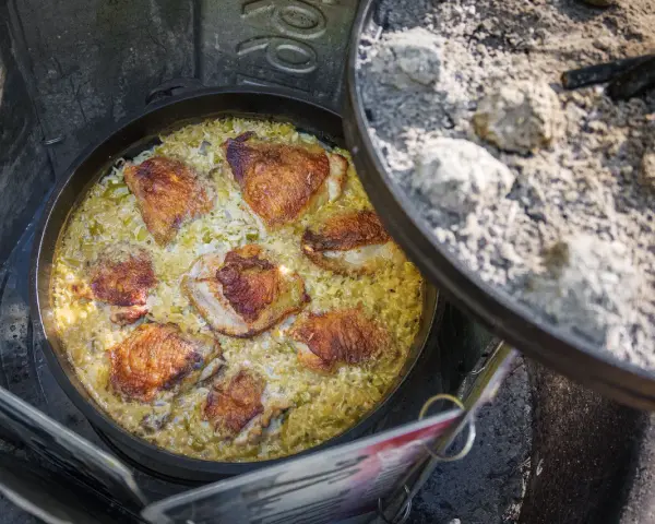 A delicious chicken and rice dish is cooking in a Dutch oven over a campfire, perfect for outdoor dutch oven campfire recipes.