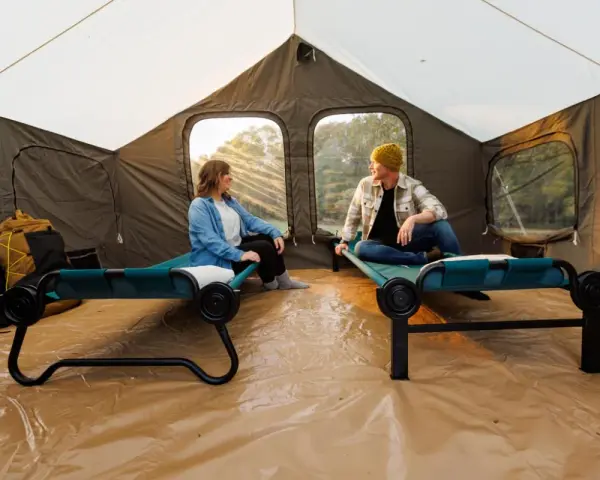Two people relax on cots inside a large tent, showcasing smart tent camping hacks for comfort and organization.