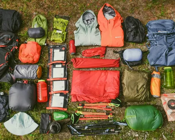 A comprehensive fastpacking gear list, including backpacks, sleeping bags, tents, jackets, food, and trekking poles, laid out on grass.
