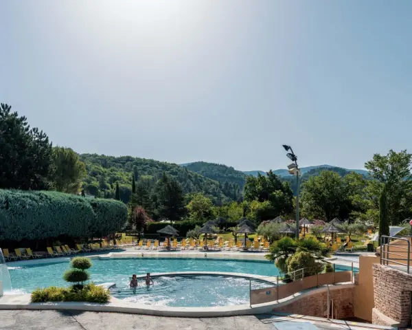 Enjoying a refreshing dip in the pool during a camping trip in Provence. Lush green hills and trees surround the sparkling water, with sun loungers and umbrellas ready for relaxation.
