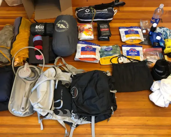 Gear laid out for beginner backpacking: tent, sleeping bag, backpack, water filter, food, and a medical kit.