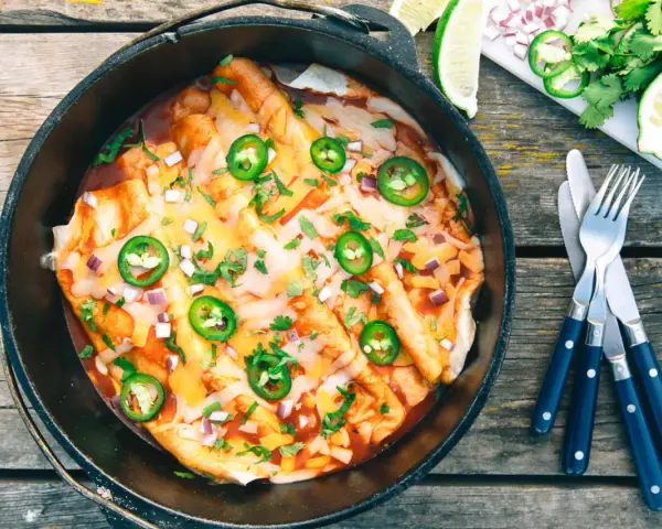 Delicious dutch oven enchiladas, topped with melted cheese, jalapeños, and cilantro, ready to be served.