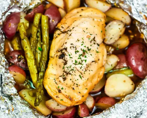 Campfire chicken foil packets in oven, with roasted potatoes and asparagus, seasoned with herbs.