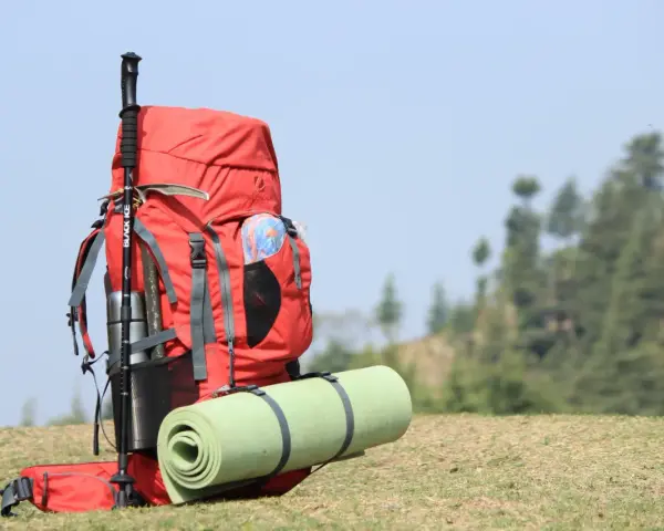 A red backpack with a rolled sleeping pad strapped to it, and trekking poles. This image shows how to pack a backpacking pack for an adventure.