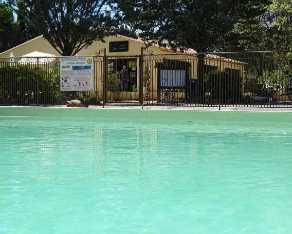 A refreshing pool awaits at this camping in Aix en Provence. A sign details pool depths, and a man stands near the reception building.