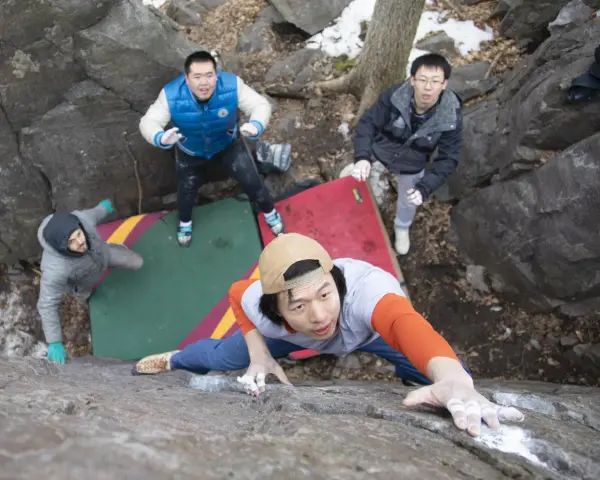 Four friends enjoy bouldering, a type of rock climbing, on a rocky outdoor course with crash pads.