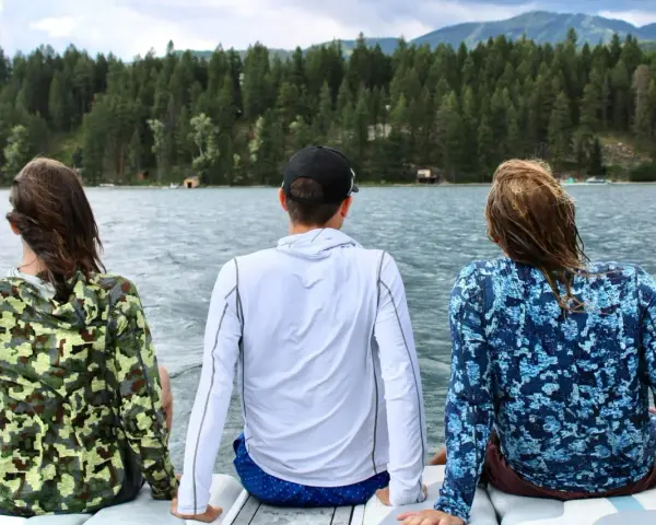 Three friends enjoy a lake view, wearing cooling clothing for extreme heat. The camouflage and blue patterned shirts offer sun protection.