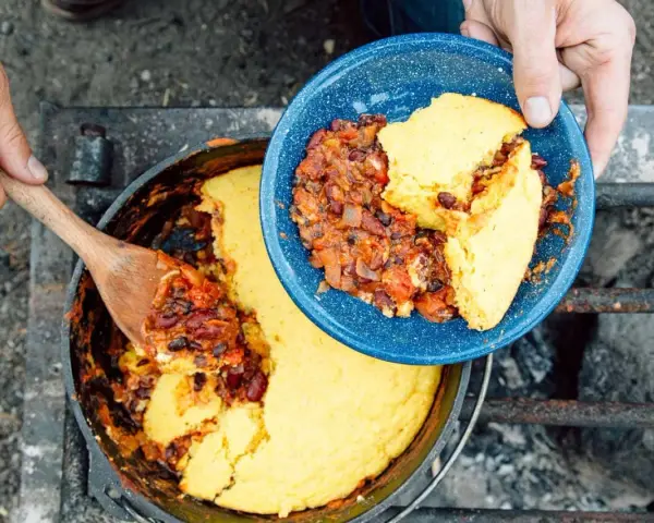 Serving hearty chili and cornbread from a Dutch oven over a campfire. This is easy camp food at its finest.