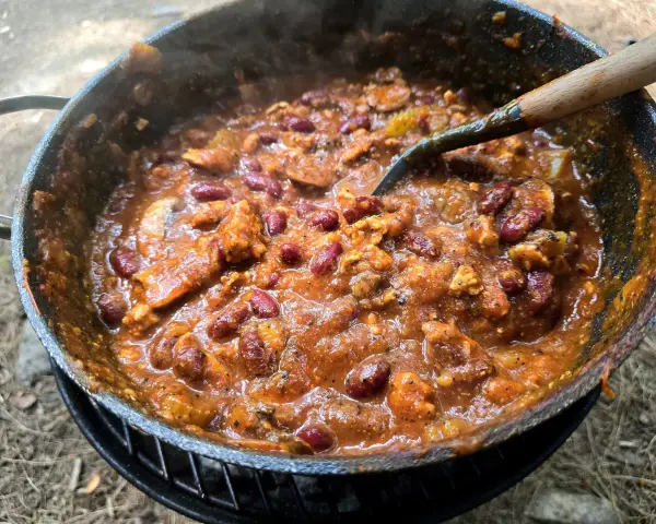 A hearty dutch oven chilli, bubbling and steaming, with kidney beans and chunks of meat, ready to be served.