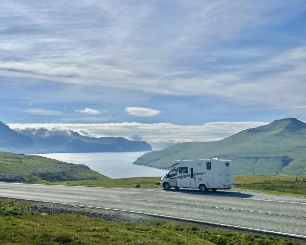 A white RV parked on a scenic road overlooking a bay and green mountains. This view is perfect for the best RV trip planner.