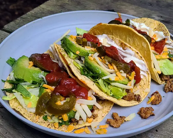 A plate of delicious camp taco with avocado, salsa, cheese, and sour cream, perfect for an outdoor meal.