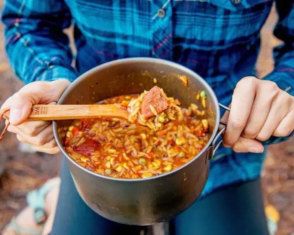 A wooden spoon scoops a hearty portion of campfire jambalaya from a pot.