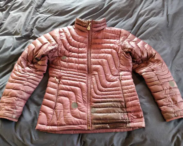 A maroon puffer jacket lies on a dark, wrinkled surface, ready for cleaning. Learn how to wash a down jacket to keep it fluffy and warm.