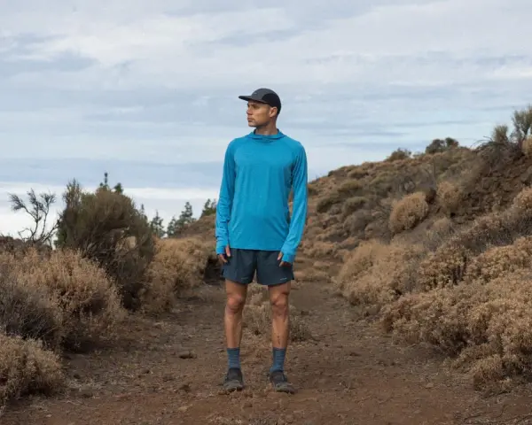 Runner in blue shirt and shorts on a dusty trail, contemplating the disadvantages of merino wool, like its tendency to hold moisture in humid conditions.