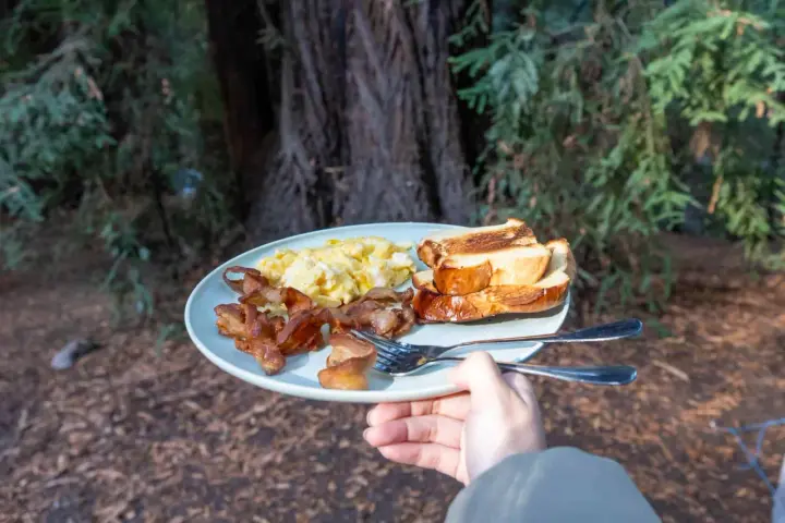 A plate of scrambled eggs, crispy bacon, and toasted bread, a delicious breakfast showcasing some great camping hacks for enjoying a hearty meal outdoors.