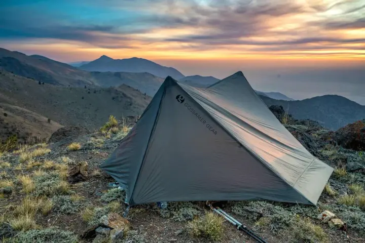 A Gossamer Gear tent sits on a rocky mountain ridge at sunset. This review highlights the gear's performance.