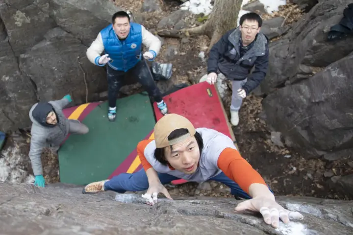 Four friends enjoy bouldering, a type of rock climbing, on a rocky outdoor course with crash pads.