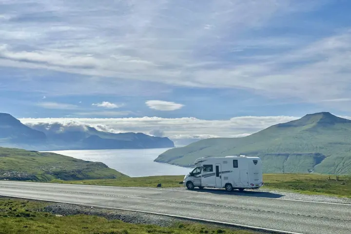 A white RV parked on a scenic road overlooking a bay and green mountains. This view is perfect for the best RV trip planner.