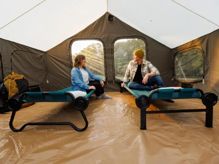Two people relax on cots inside a large tent, showcasing smart tent camping hacks for comfort and organization.
