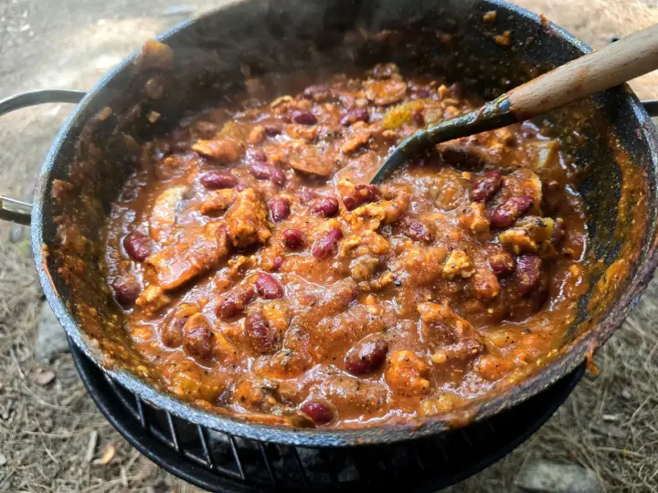 A hearty dutch oven chilli, bubbling and steaming, with kidney beans and chunks of meat, ready to be served.