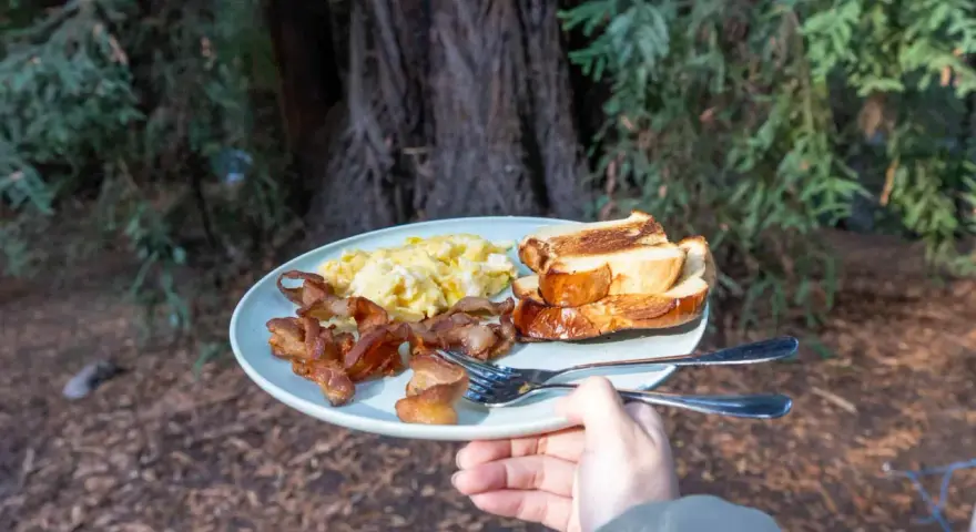 A plate of scrambled eggs, crispy bacon, and toasted bread, a delicious breakfast showcasing some great camping hacks for enjoying a hearty meal outdoors.
