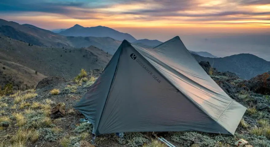 A Gossamer Gear tent sits on a rocky mountain ridge at sunset. This review highlights the gear's performance.