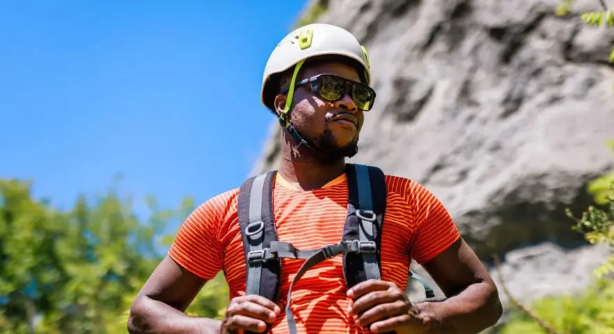 A man in a helmet and sunglasses pauses during a hike in hot weather, ready for his next climb.