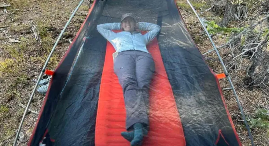 A person relaxes inside a tent on a bright orange Therm-a-Rest NeoAir XLite sleeping pad, enjoying the outdoors.