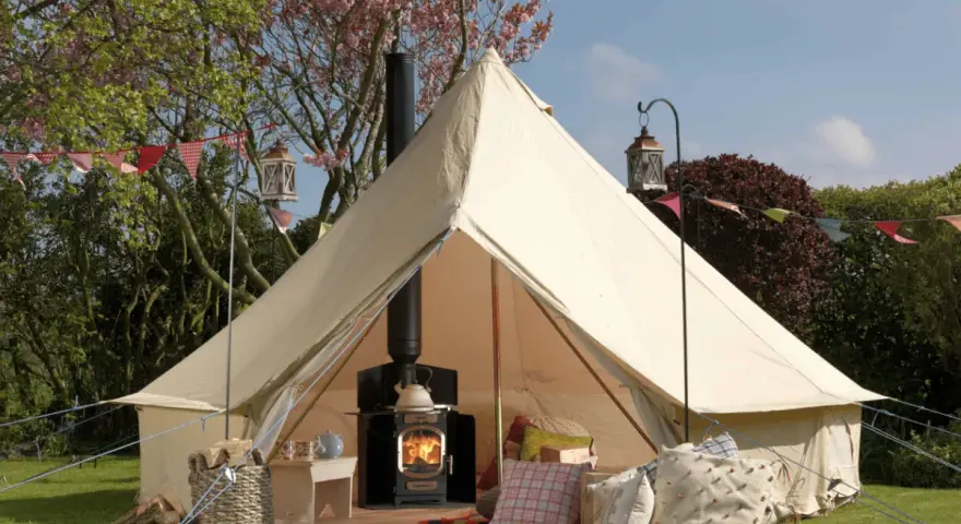 A cozy bell tent with a wood-burning stove inside, showcasing what is glamping: comfort and nature combined.