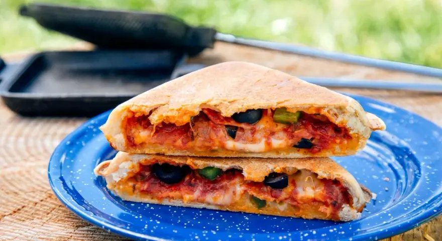 A delicious pie iron pizza, cut in half and stacked, reveals melted cheese, pepperoni, olives, and peppers.