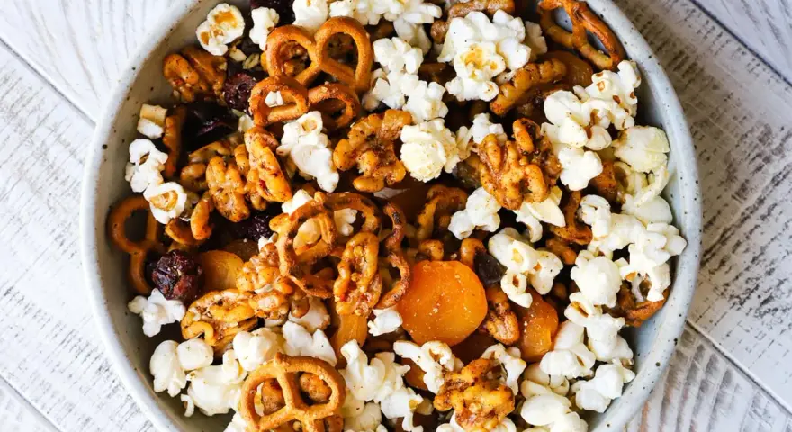 A bowl of delicious walnut trail mix, featuring popcorn, pretzels, dried cranberries, and apricots.