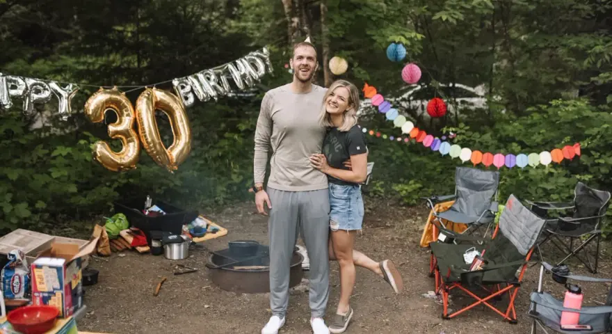 Couple celebrates 30th birthday with fun camping birthday ideas. Balloons and colorful banners decorate the campsite.