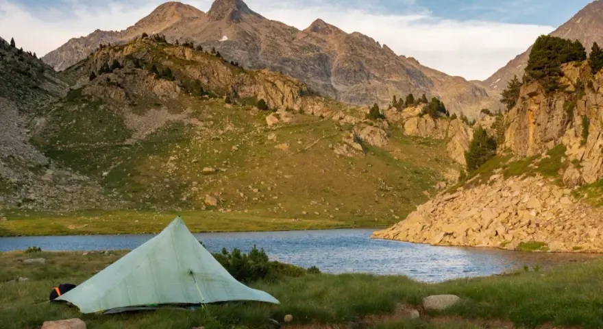 A tent sits by a serene lake, with rugged mountains in the background, a perfect campsite on the Pyrenees High Route.