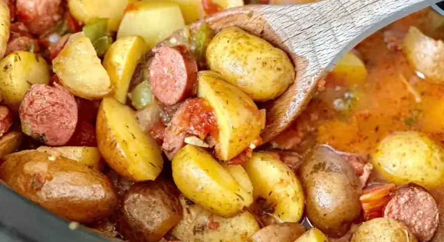 A wooden spoon scoops up hearty potatoes and sausage from a crockpot, perfect for camping crockpot meals.