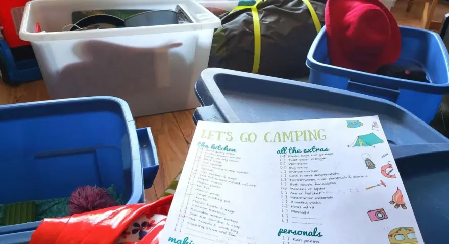 A "Let's Go Camping" checklist is spread out among blue and white storage bins, ready for a trip.