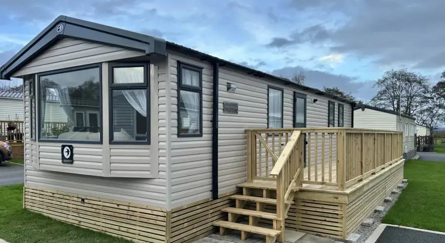 A beige Swift Provence mobil home with a wooden deck and steps. This idyllic location in Provence offers a cozy getaway.