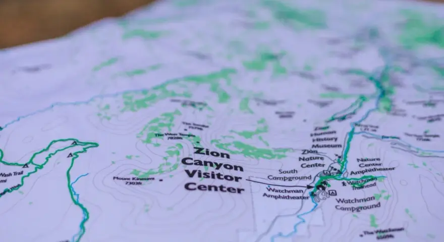 A topographic map of Zion Canyon shows elevation changes with contour lines, highlighting trails, visitor centers, and campgrounds.