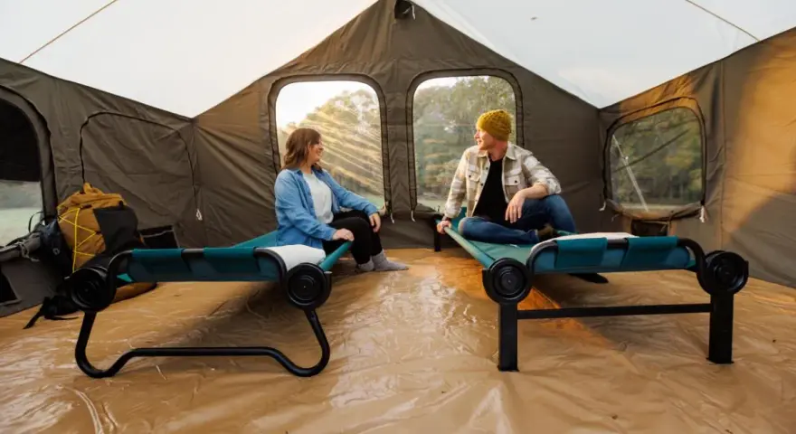 Two people relax on cots inside a large tent, showcasing smart tent camping hacks for comfort and organization.